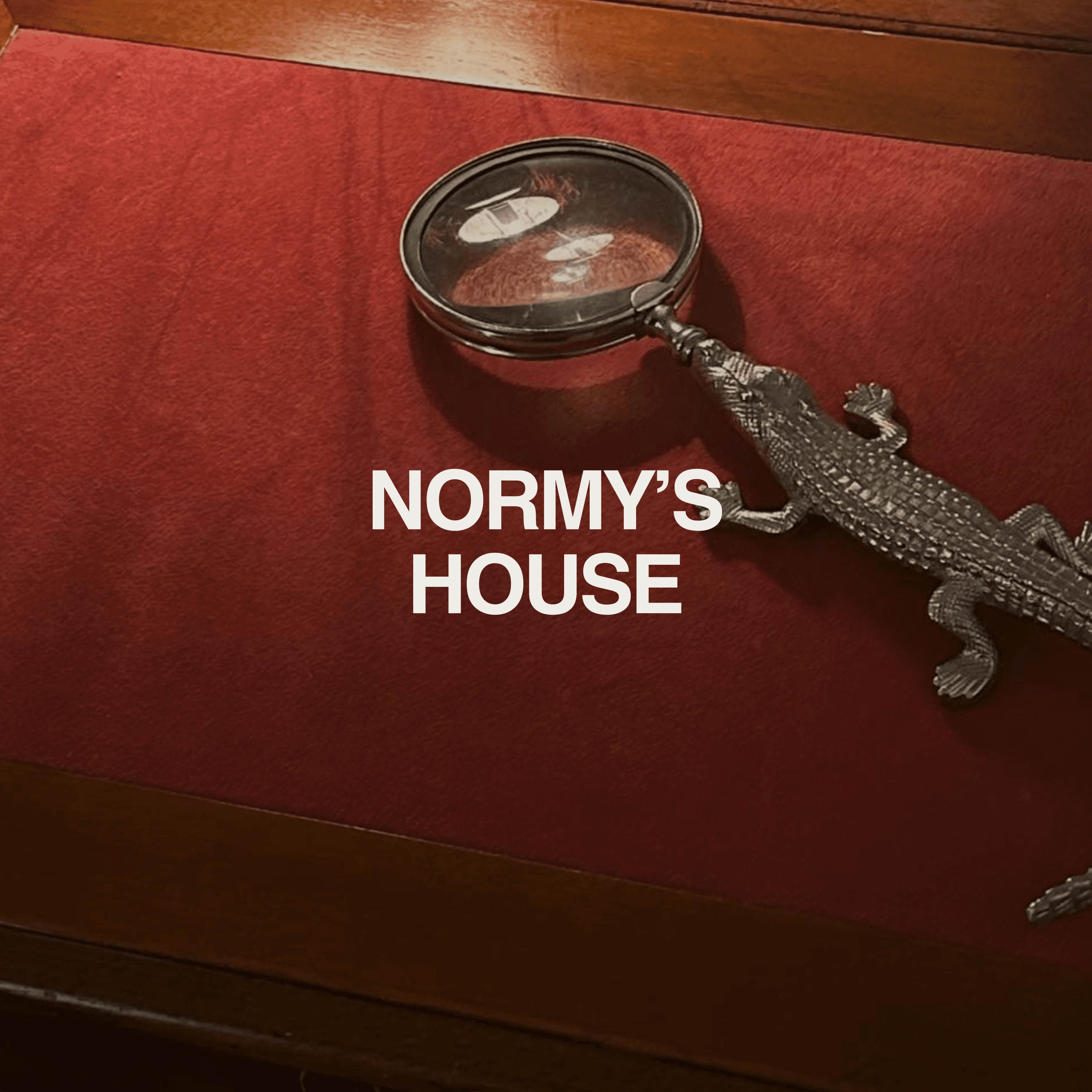 Vintage magnifying glass and silver lizard on dark wood table with red felt, evoking nostalgic, old-world charm of Grandpa’s house—Normy Playlist cover.