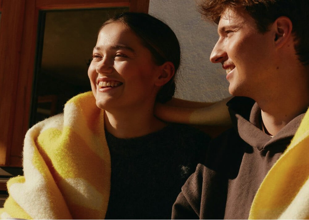 Two people sitting together indoors, smiling.