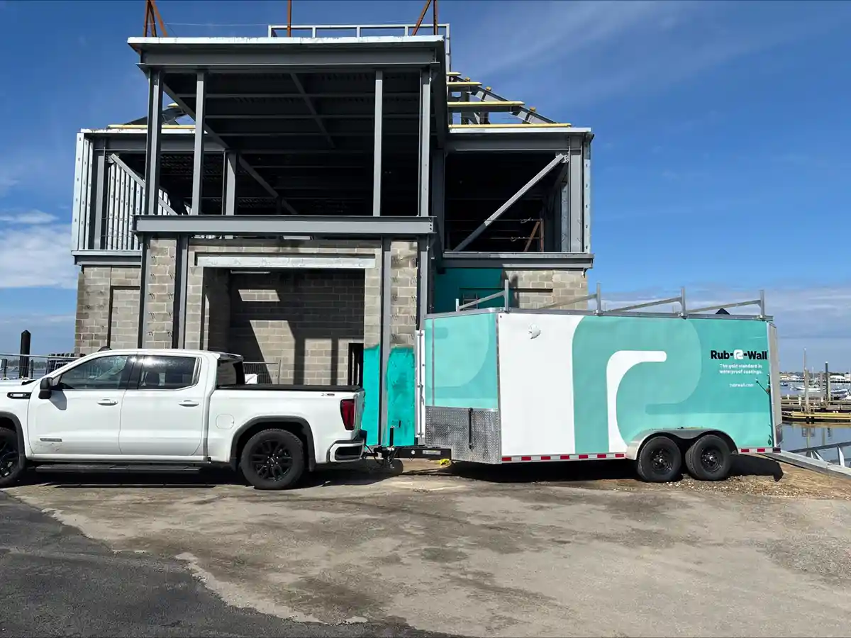 A waterproofing truck towing a Rub-R-Wall applicator trailer on a jobsite