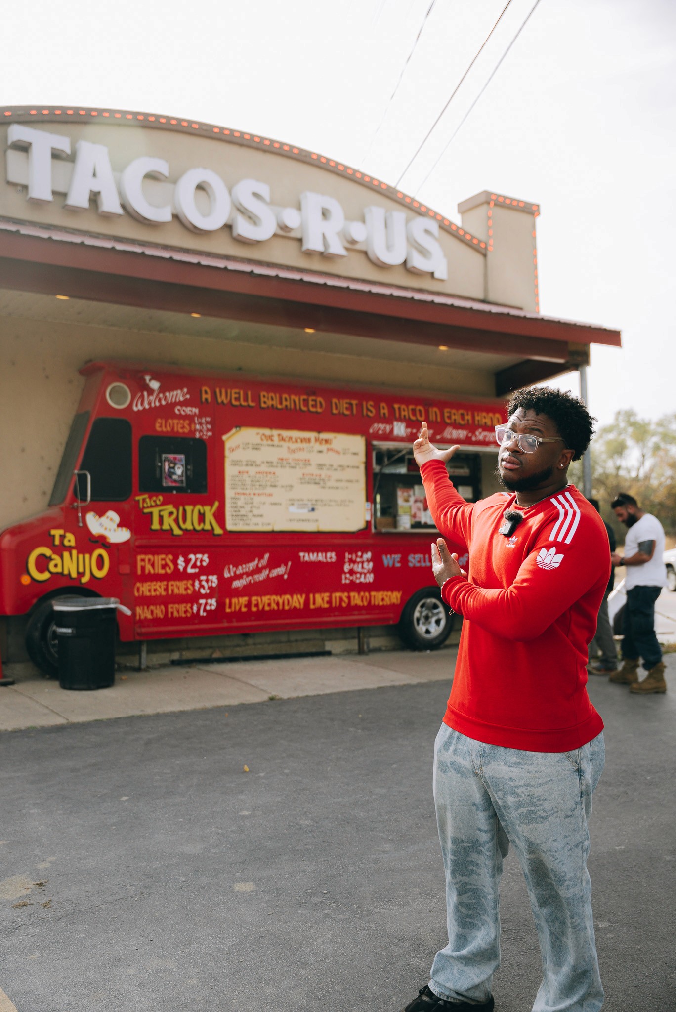 Two smiling people outdoors, one in a pink jacket holding a white phone, the other in blue with a buzz cut holding a blue phone, under a clear sky.