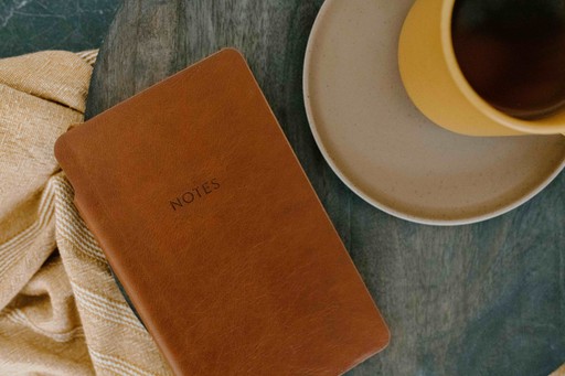 Orange leather bound journal placed next to yellow coffee cup.