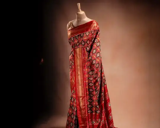 An orange Ikat saree from That Saree Shop draped on a mannequin, displaying its handwoven geometric patterns and rich traditional craftsmanship in vibrant hues.