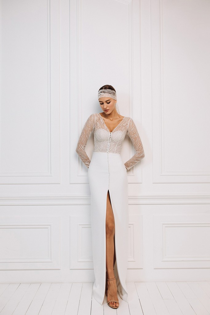 Elegante moderne trouwjurk met transparante tule mouwen en diepe halslijn, verkrijgbaar voor verhuur bij Magnolia Bruidsatelier in Deventer.