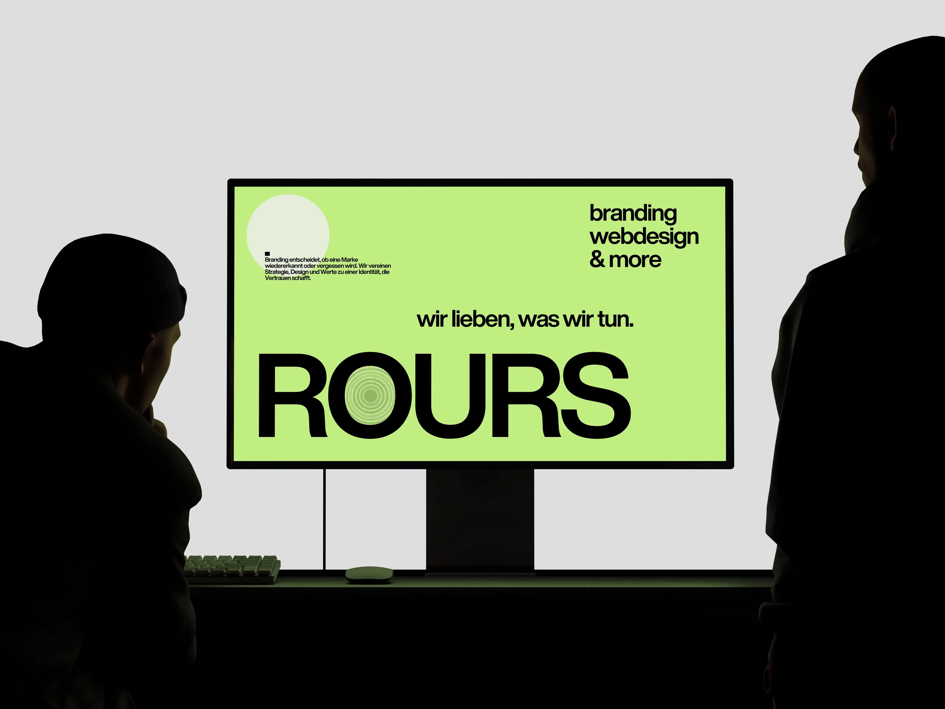 Zwei Personen stehen vor einem Monitor mit einer Branding- und Webdesign-Website im minimalistischen Design mit dem Schriftzug ROURS.
