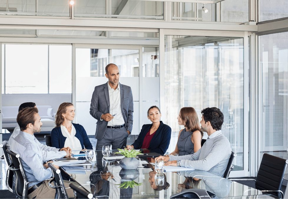 A diverse group of business professionals engaged in a meeting around a modern glass conference table in an office setting, illustrating a dynamic enterprise environment.