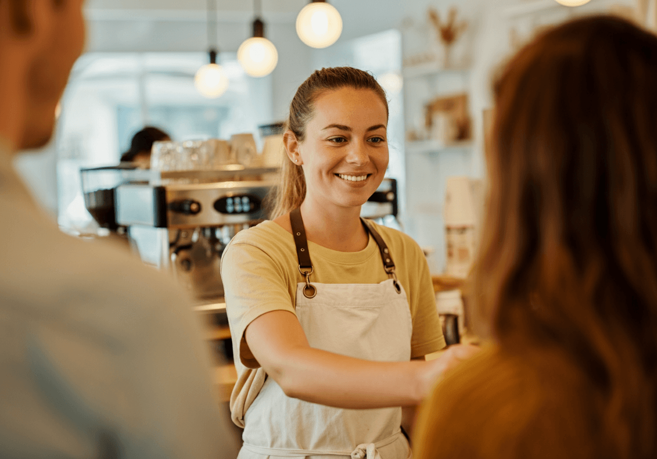 Barista handing a coffee to customers in a cosy cafe