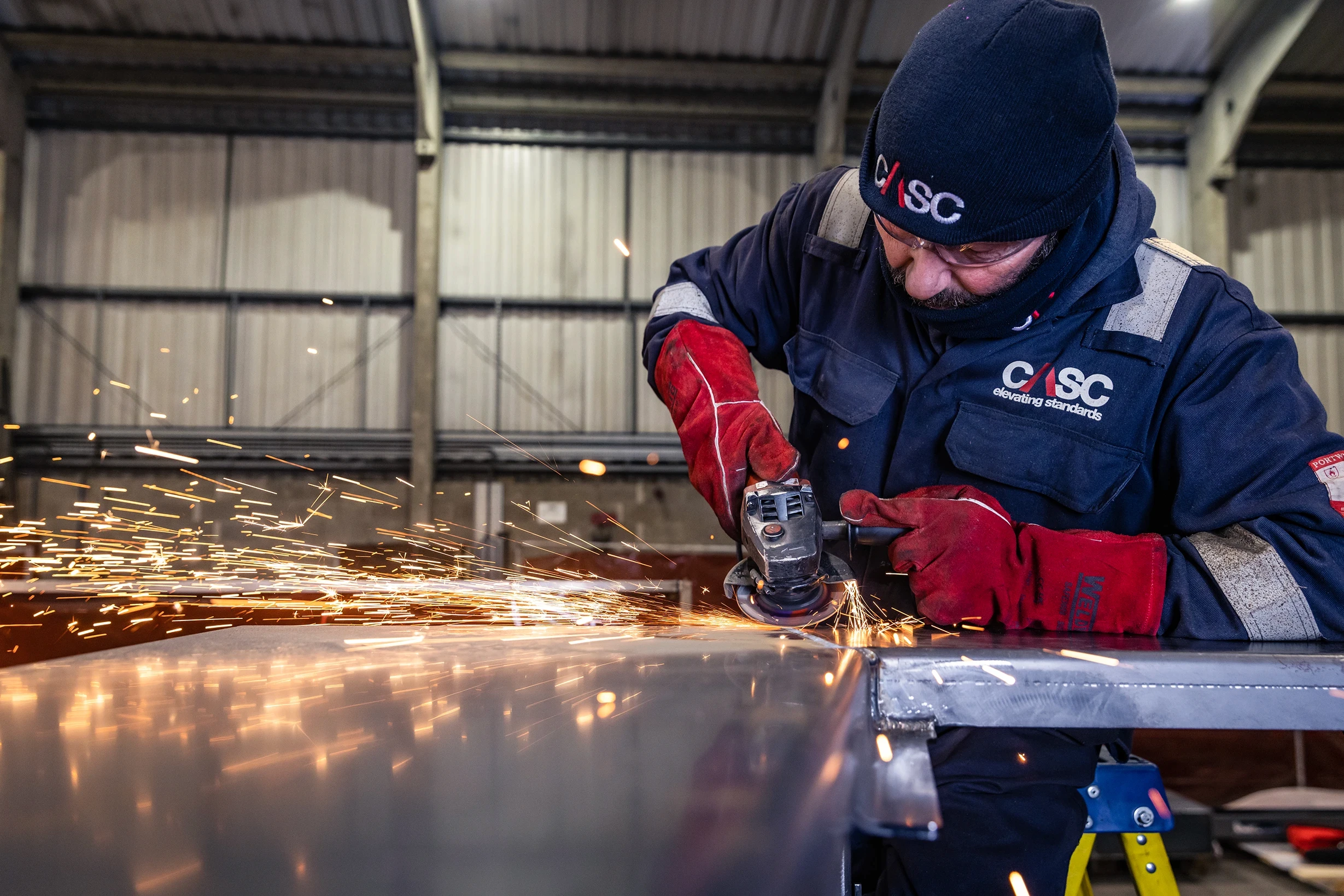 Engineer grinding and finishing a steel component in a fabrication workshop, with sparks flying from an angle grinder.