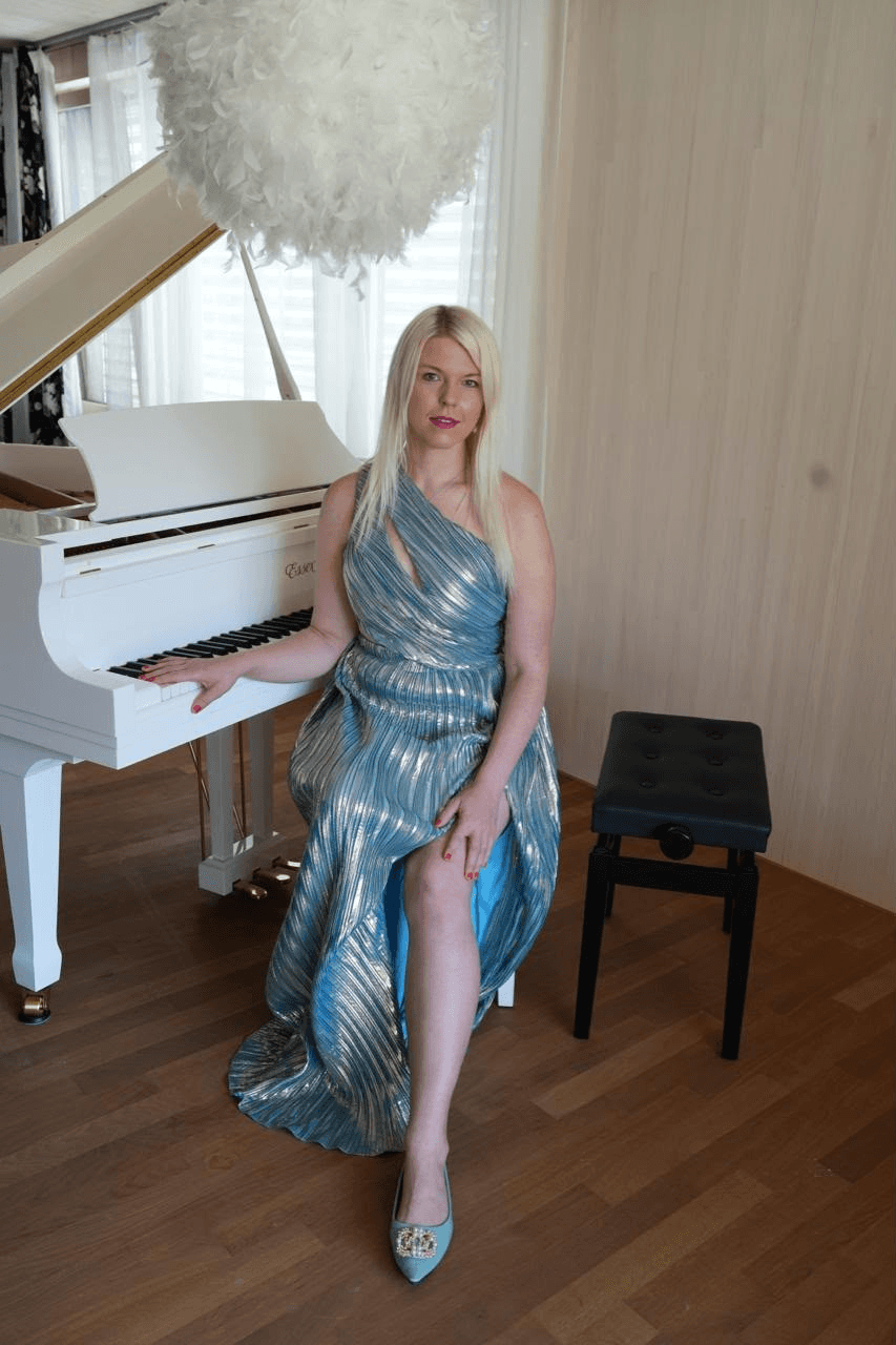 Ellen Fischerová in a shimmering blue gown seated beside a white grand piano.