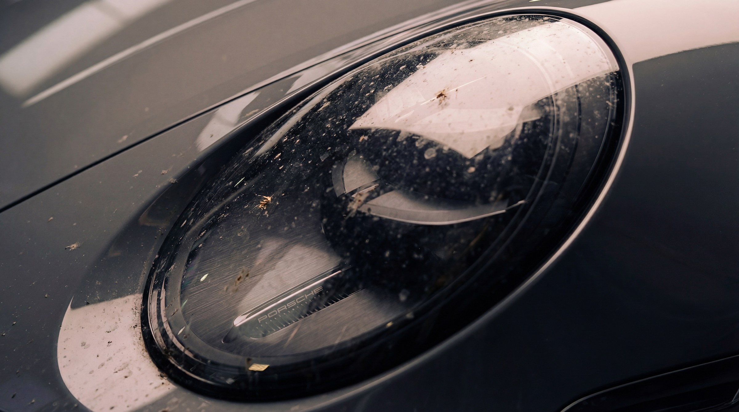 Avant nettoyage du phare avant d’une Porsche 911 avec traces et dépôts