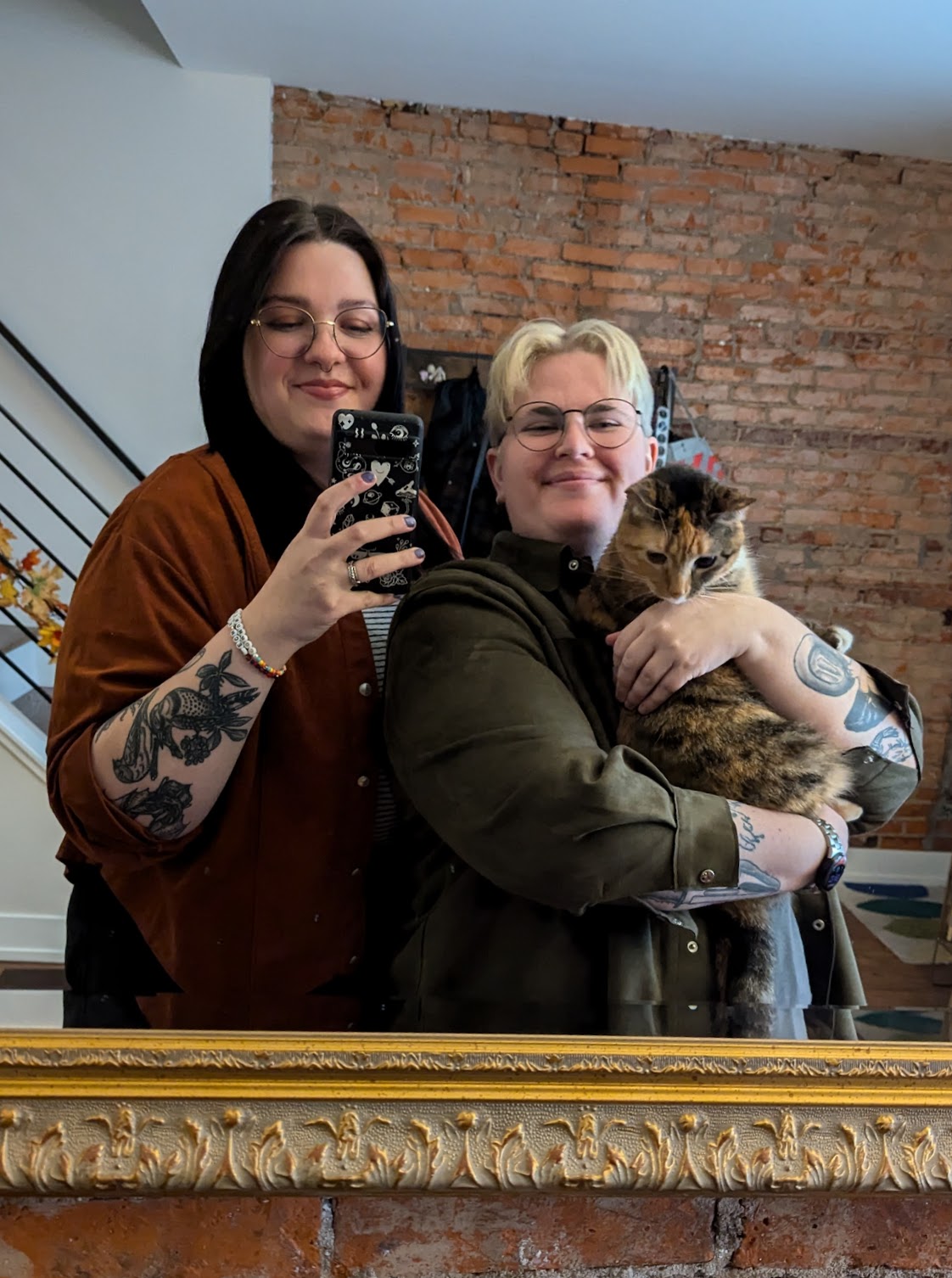 My wife and I smiling, taking a mirror selfie. I'm holding our cat and she is less than enthused about the whole thing.