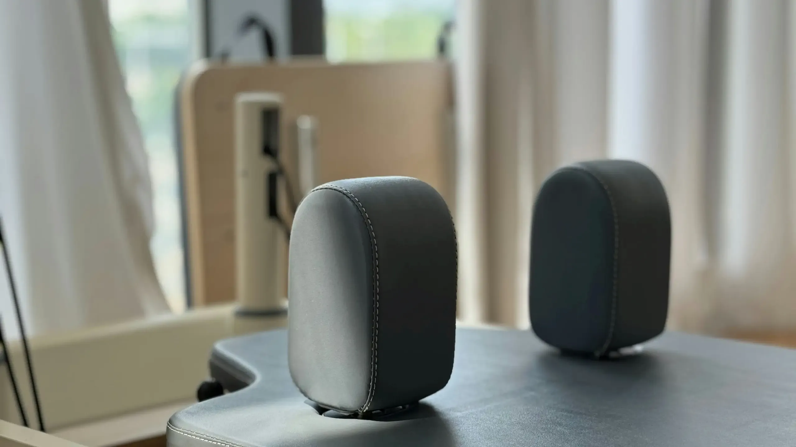 Nahaufnahme schwarzer Leder-Kopfstütze am Pilates Reformer mit unscharfem Holz-Geräteständer im Hintergrund eines Wellness-Studios