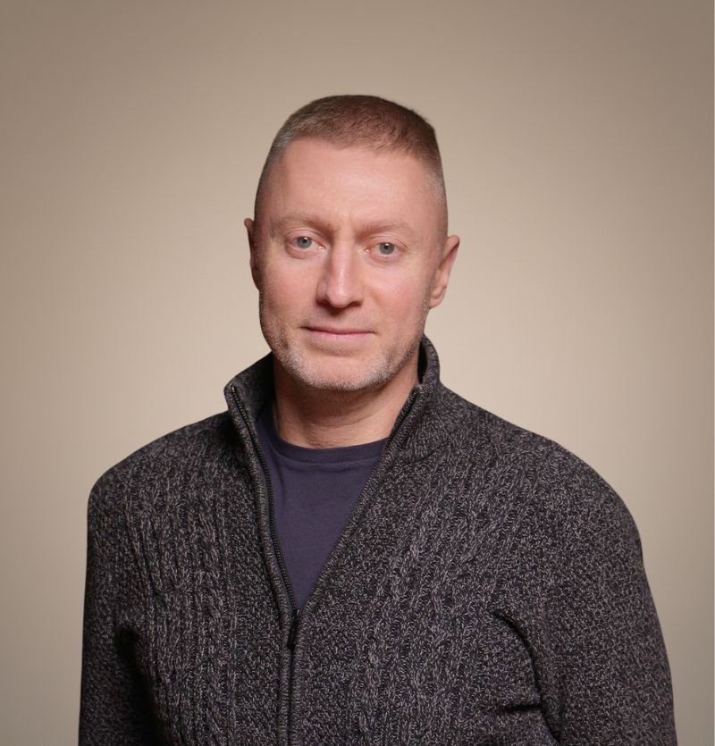 A confident person with short, styled hair and a leather jacket poses against a dark backdrop.