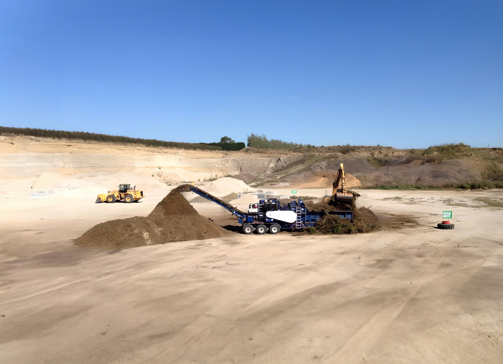 Green waste being mulched in a sand quarry with a digger and a loader