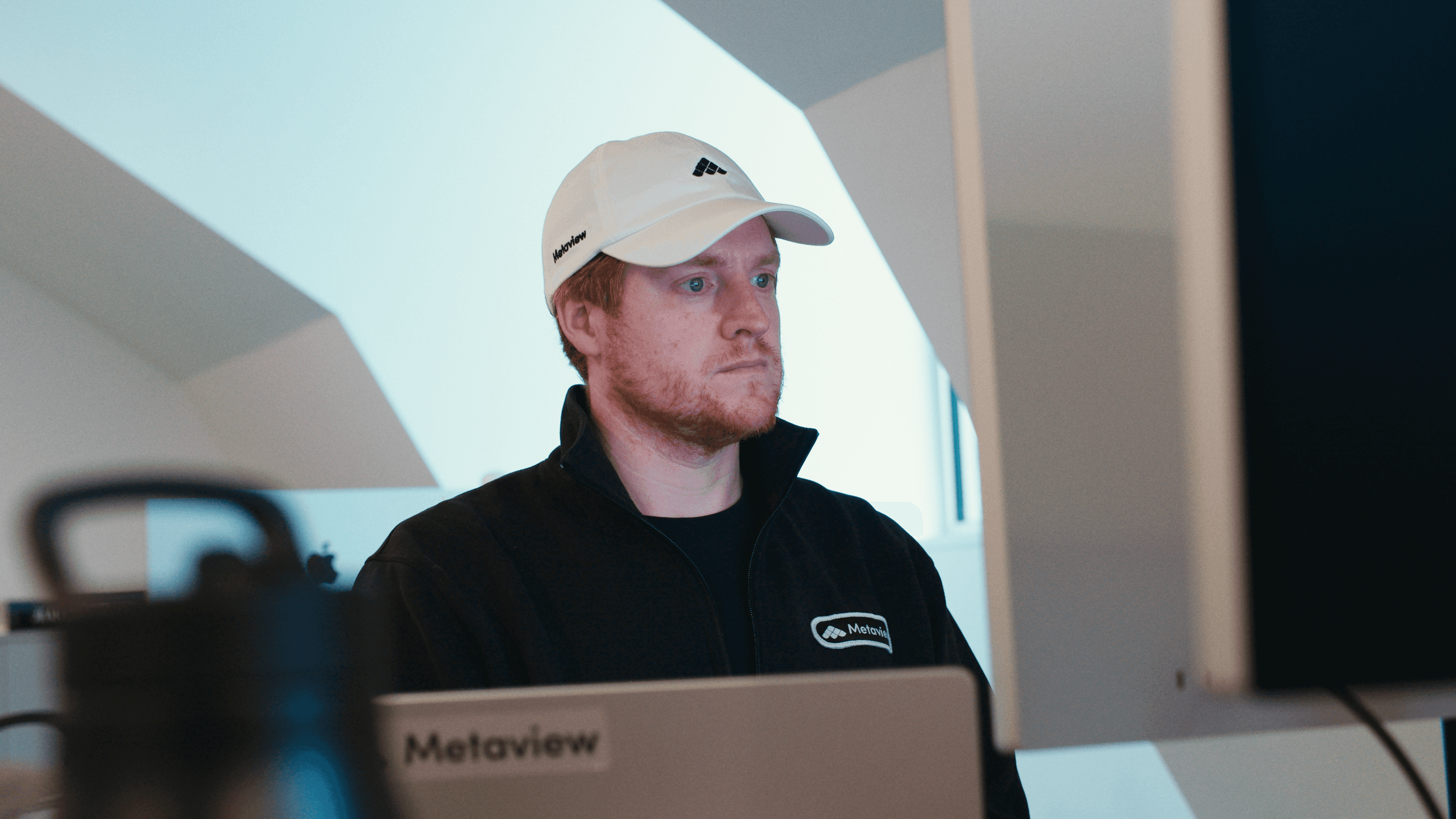 Metaview employee wearing a custom branded cap and jacket, with a Metaview sticker on their laptop