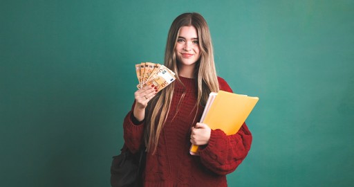 A woman with long hair holds a drink and a folder, smiling against a solid teal background.