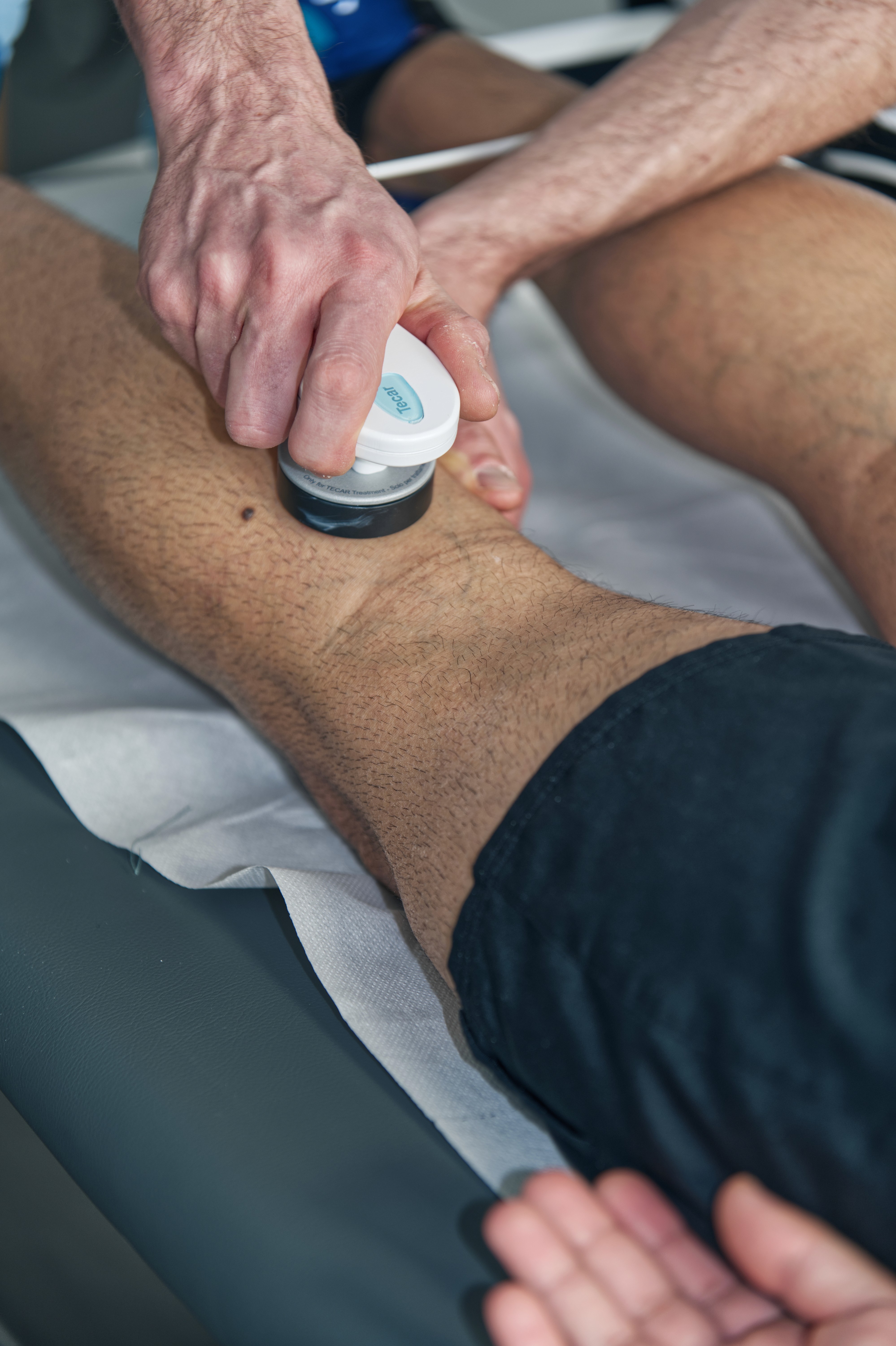 A person sits at a cluttered desk in a dimly lit room, focused on two monitors displaying aerial maps. The walls are covered with various images and notes.