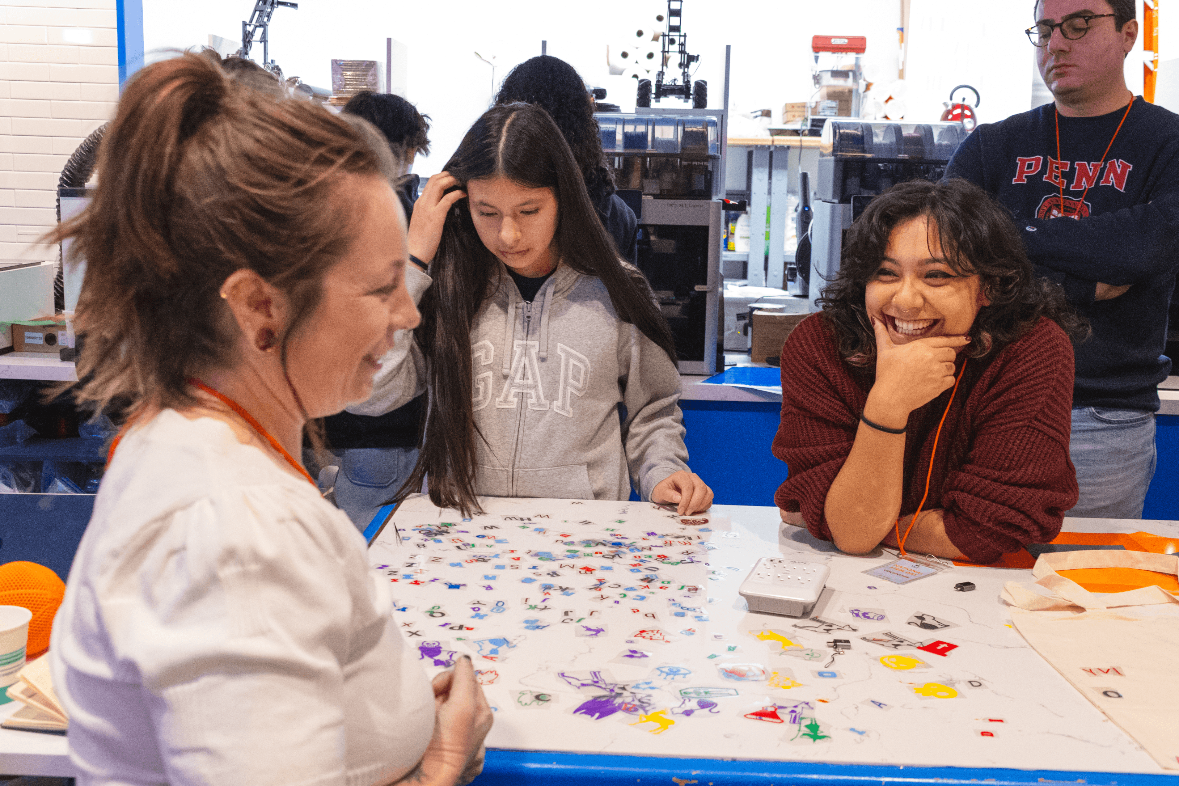Volunteers and participants laugh over a table filled with stickers and iron on patches for a tote decorating activity.