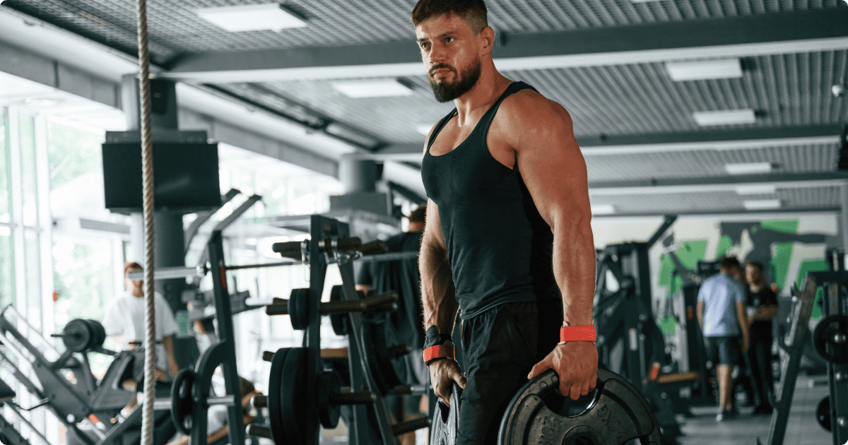 A muscular man in a gym holding two weight plates, one in each hand, as part of his workout.