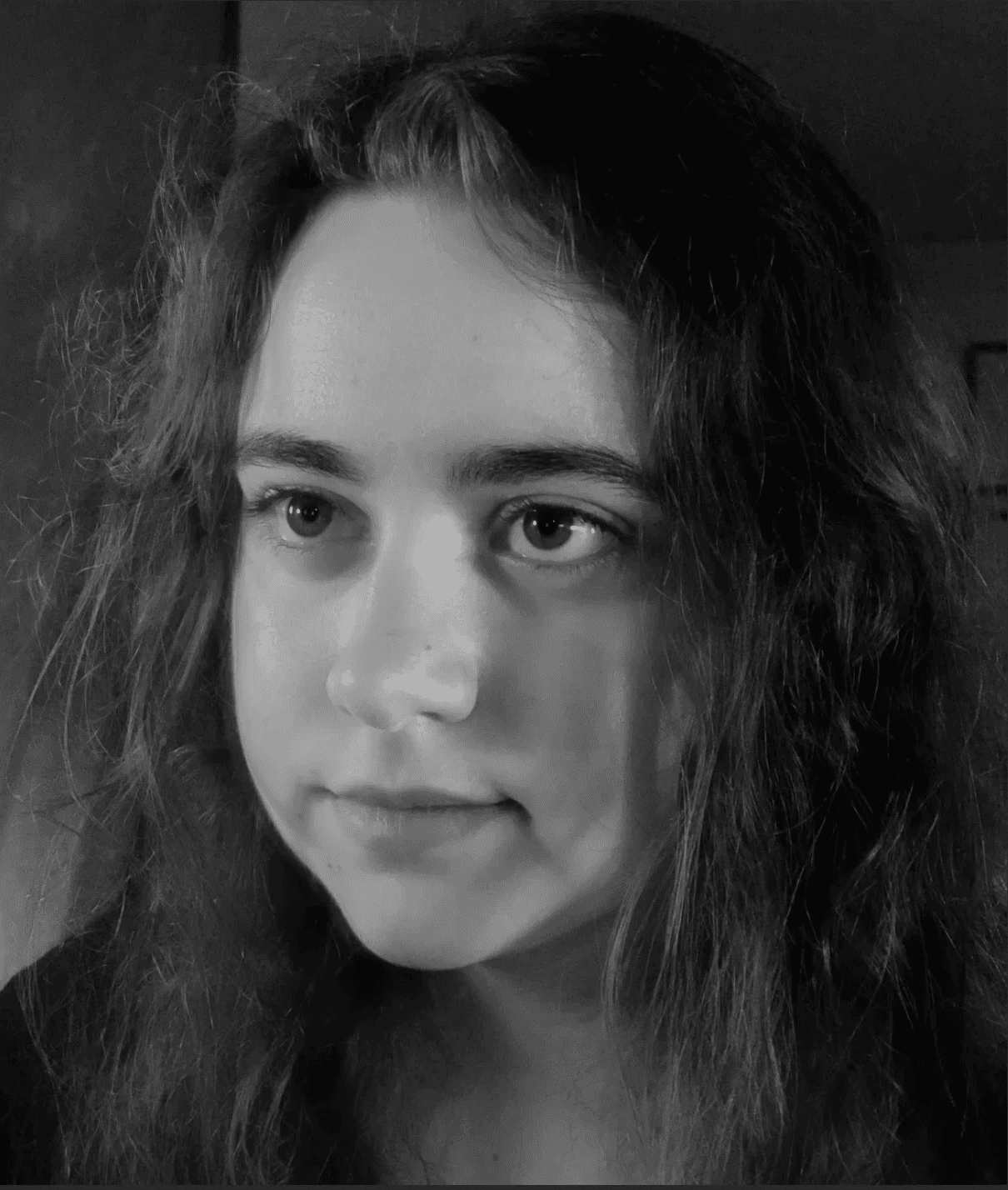 A thoughtful young person with dark hair gazes to the side, captured in soft black and white lighting.