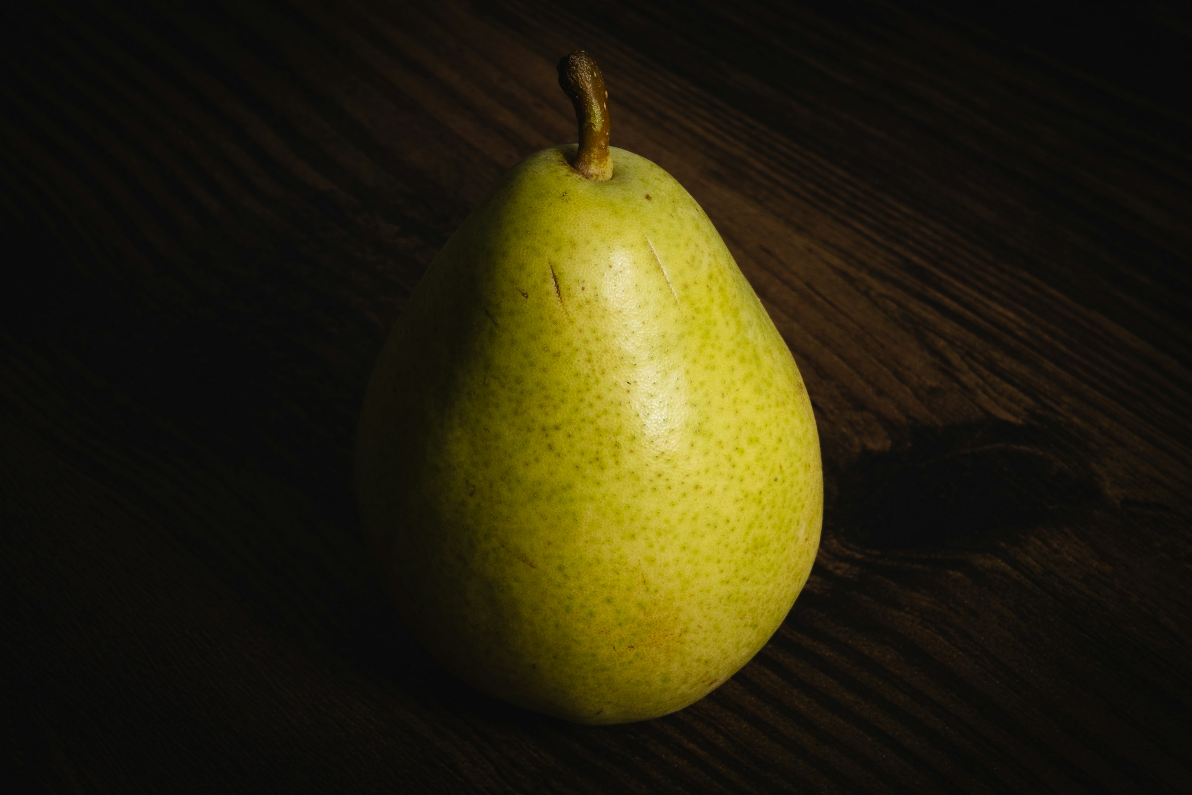 A pear on a dark wooden table in low side light