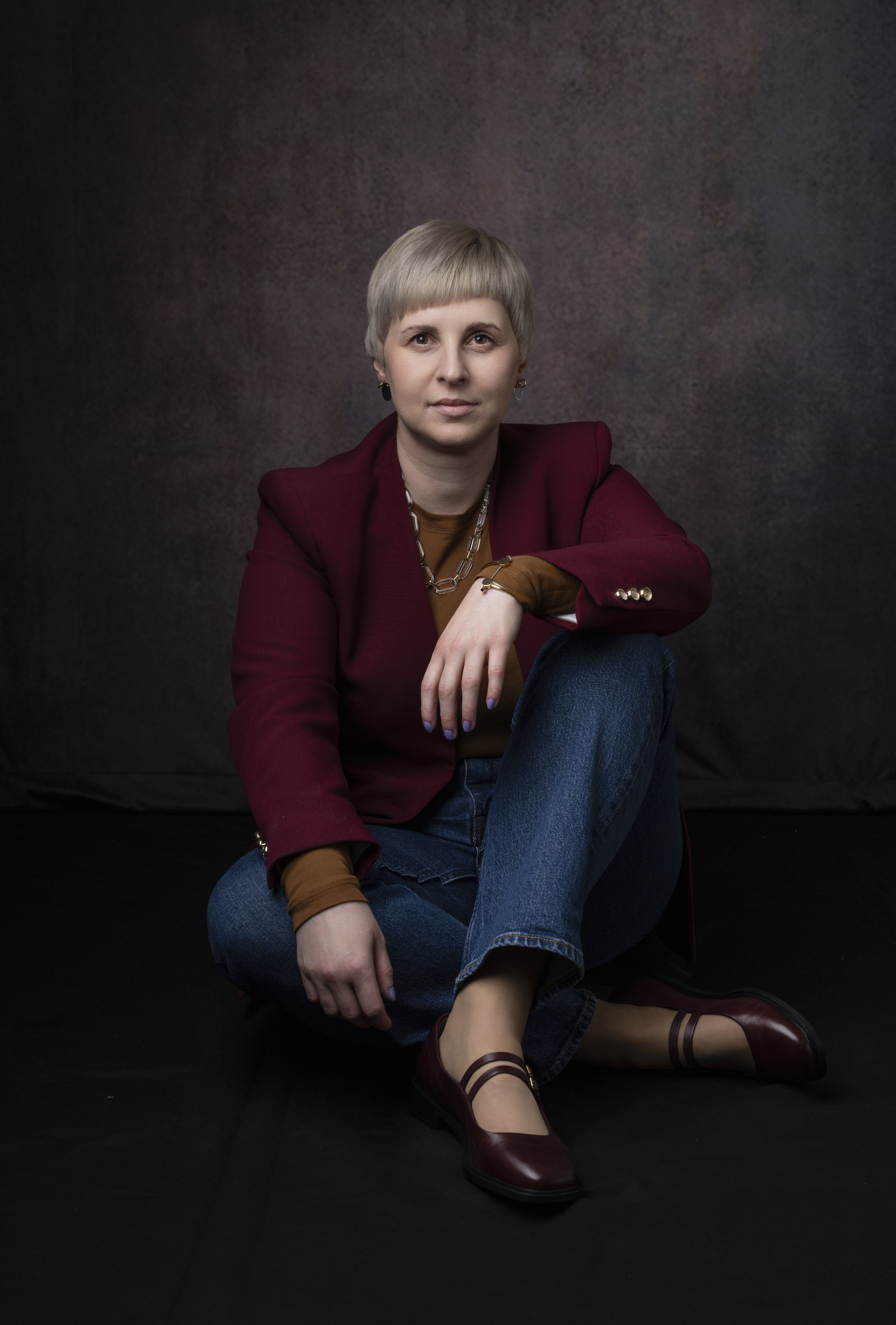 Founder portrait. Professional woman in blazer and jeans sitting cross-legged on the floor.