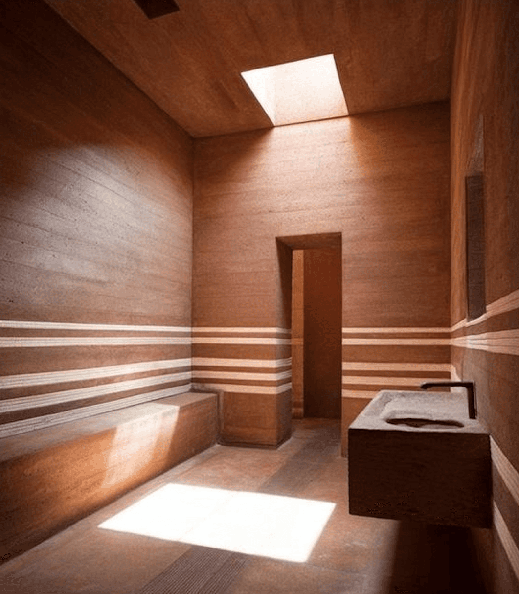 Warm-toned corridor with terracotta walls, horizontal light and shadow striping, curved architectural details, and doorway leading to adjacent room