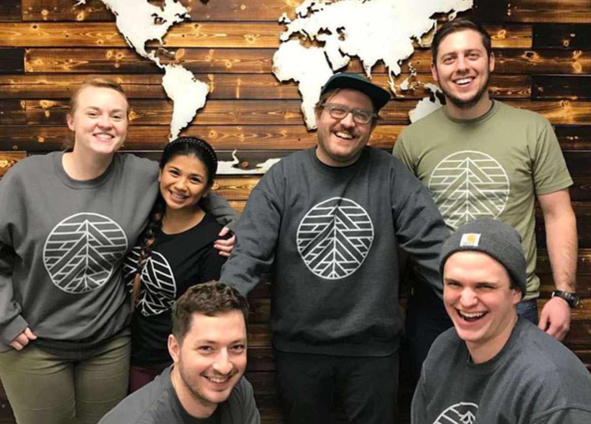 Smiling team in branded shirts against wood wall with world map.