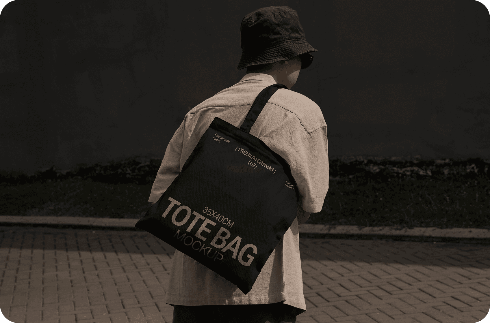 Person in a beige shirt and bucket hat carrying a black tote bag mockup outdoors.      Like  Dislike