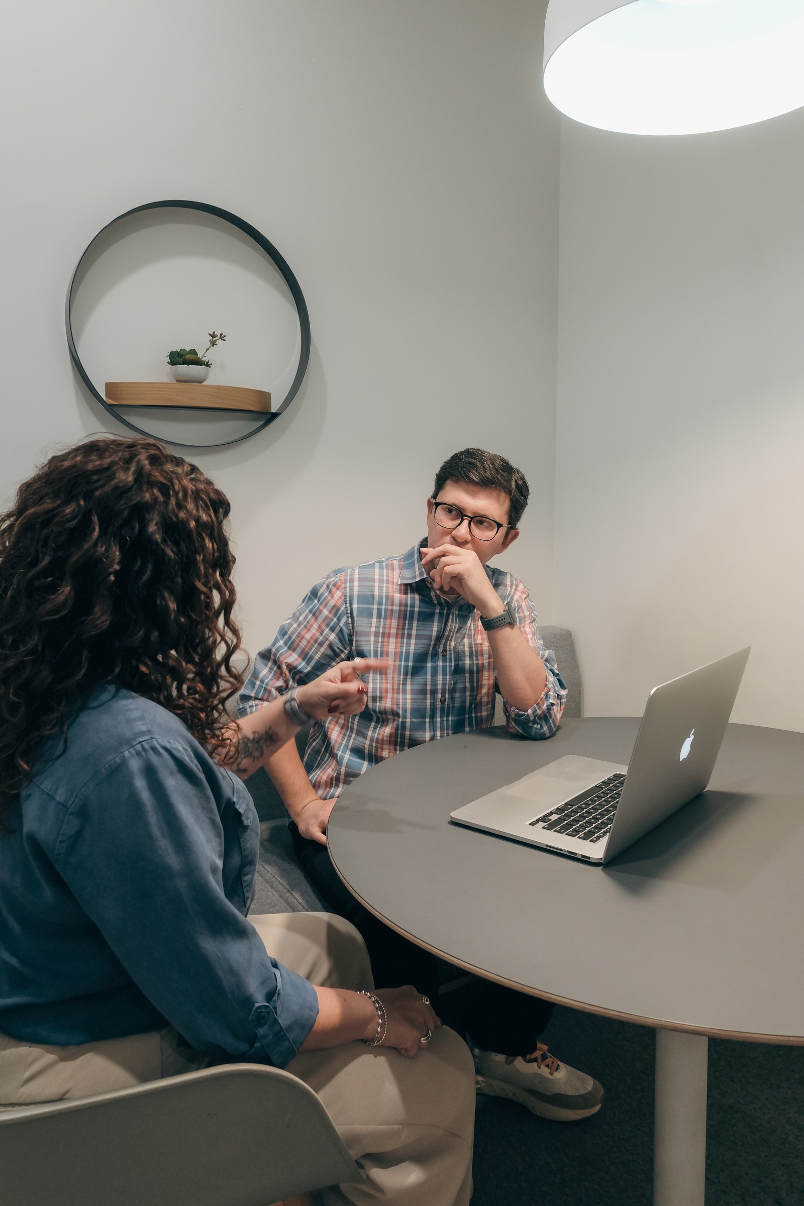 Two colleagues discussing a project at a round table with a laptop open between them.