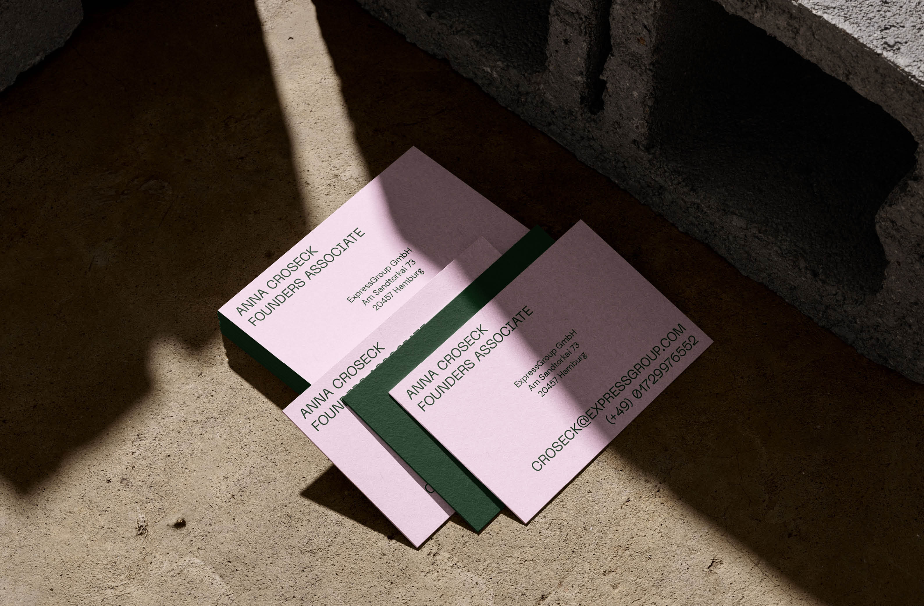 Pink and green business cards arranged on a concrete surface with dramatic lighting.