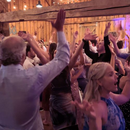 Guests at a wedding reception joyously dancing, the room filled with multicolored lighting, creating an enchanting and celebratory mood.