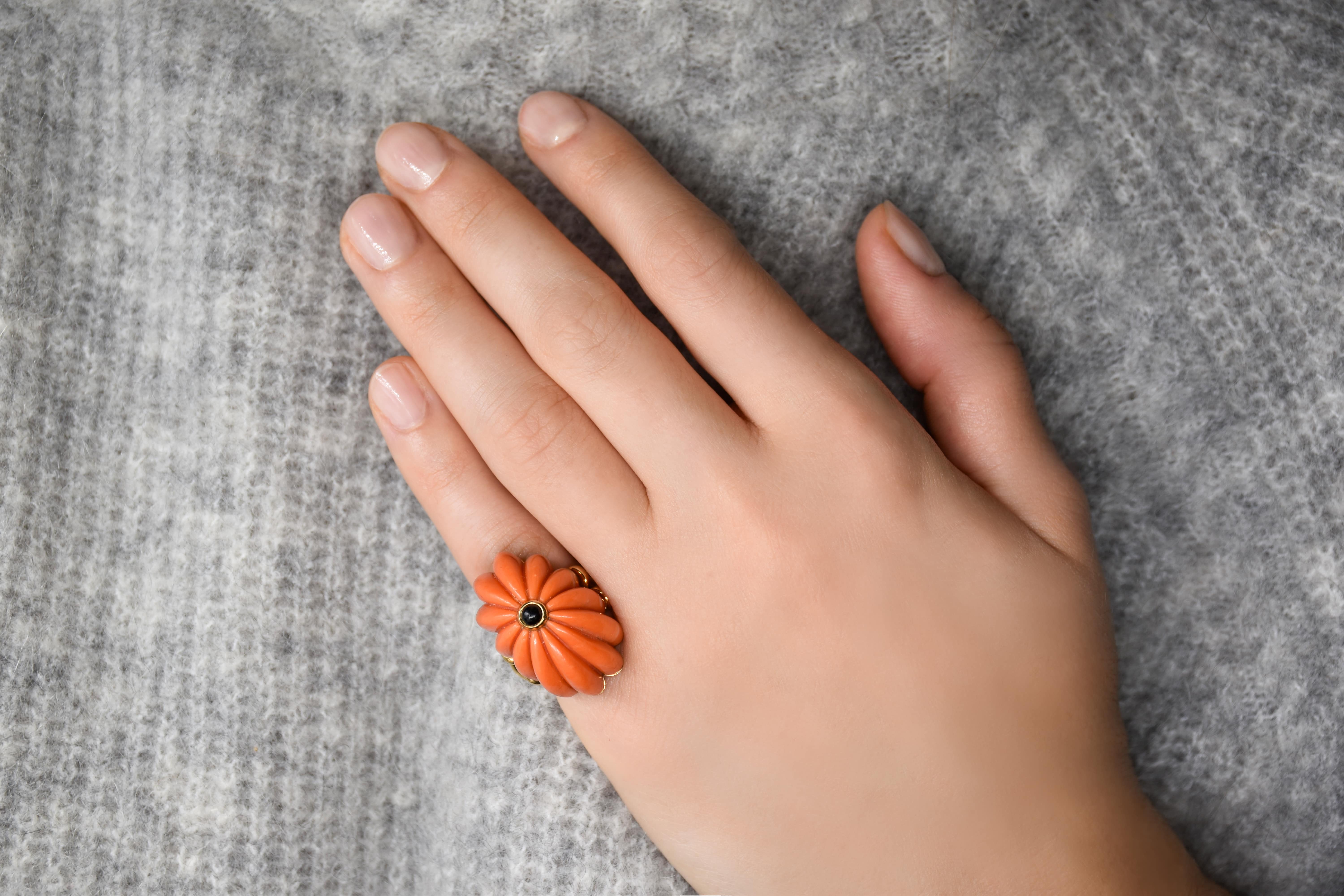 Vue portée d'une bague Chaumet en corail en forme de fleur avec un petit cabochon d'onyx sur le dessus 