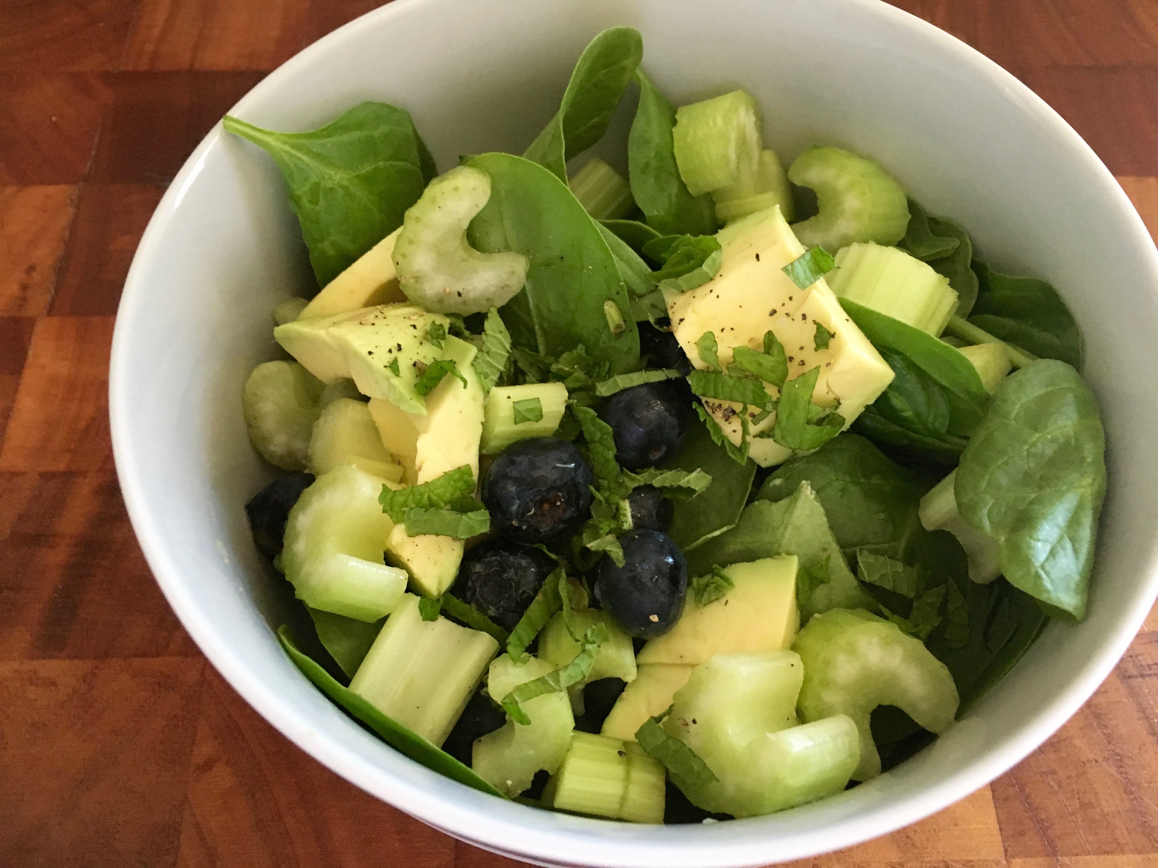 A bowl of fresh salad with chopped green vegetables, including lettuce, celery, and black olives on a wooden surface.