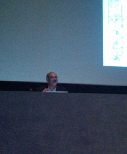 A photo of a person sitting at a desk in front of a cinema projection.