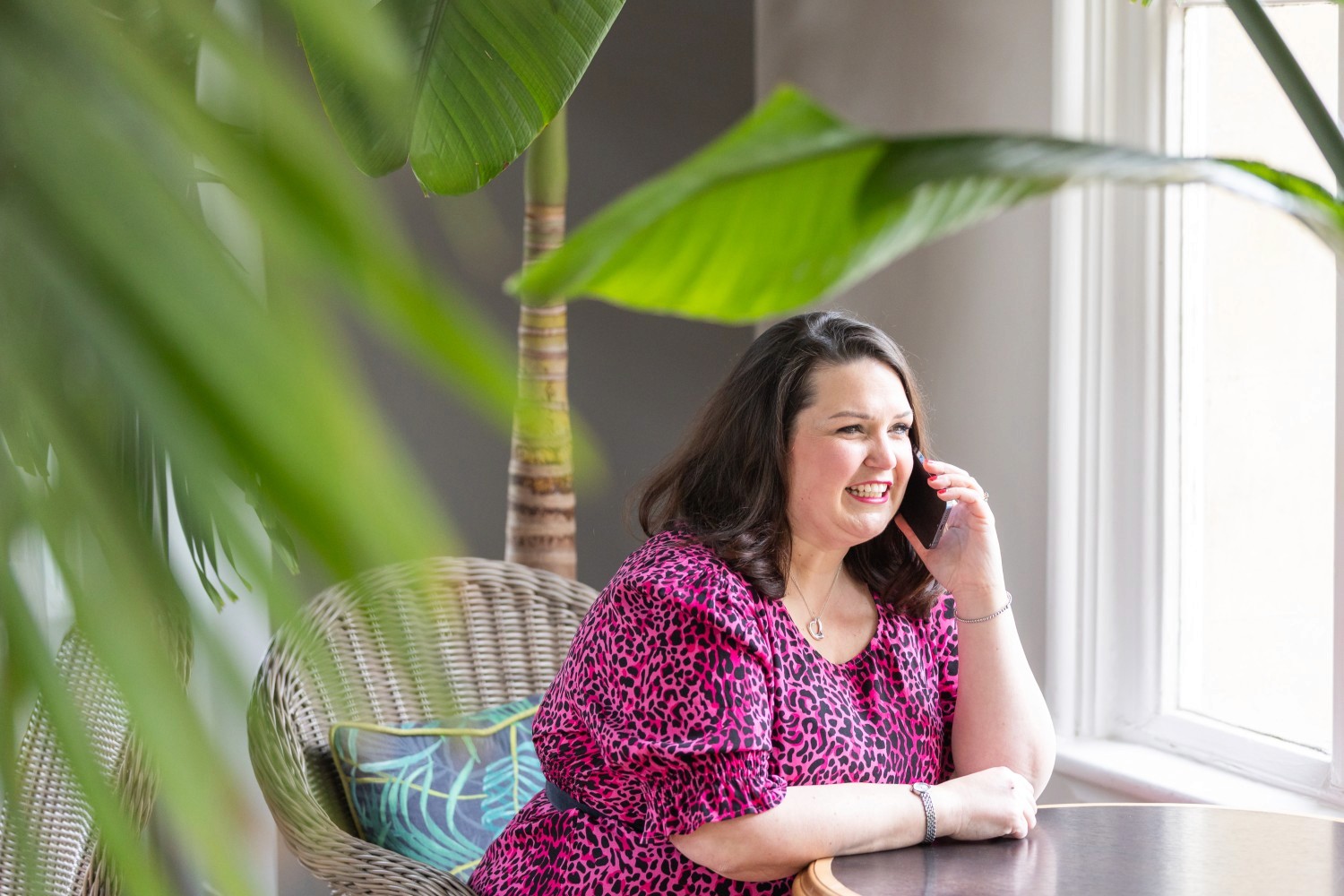 Lucy, framed by green leaves, on the phone, smiling.