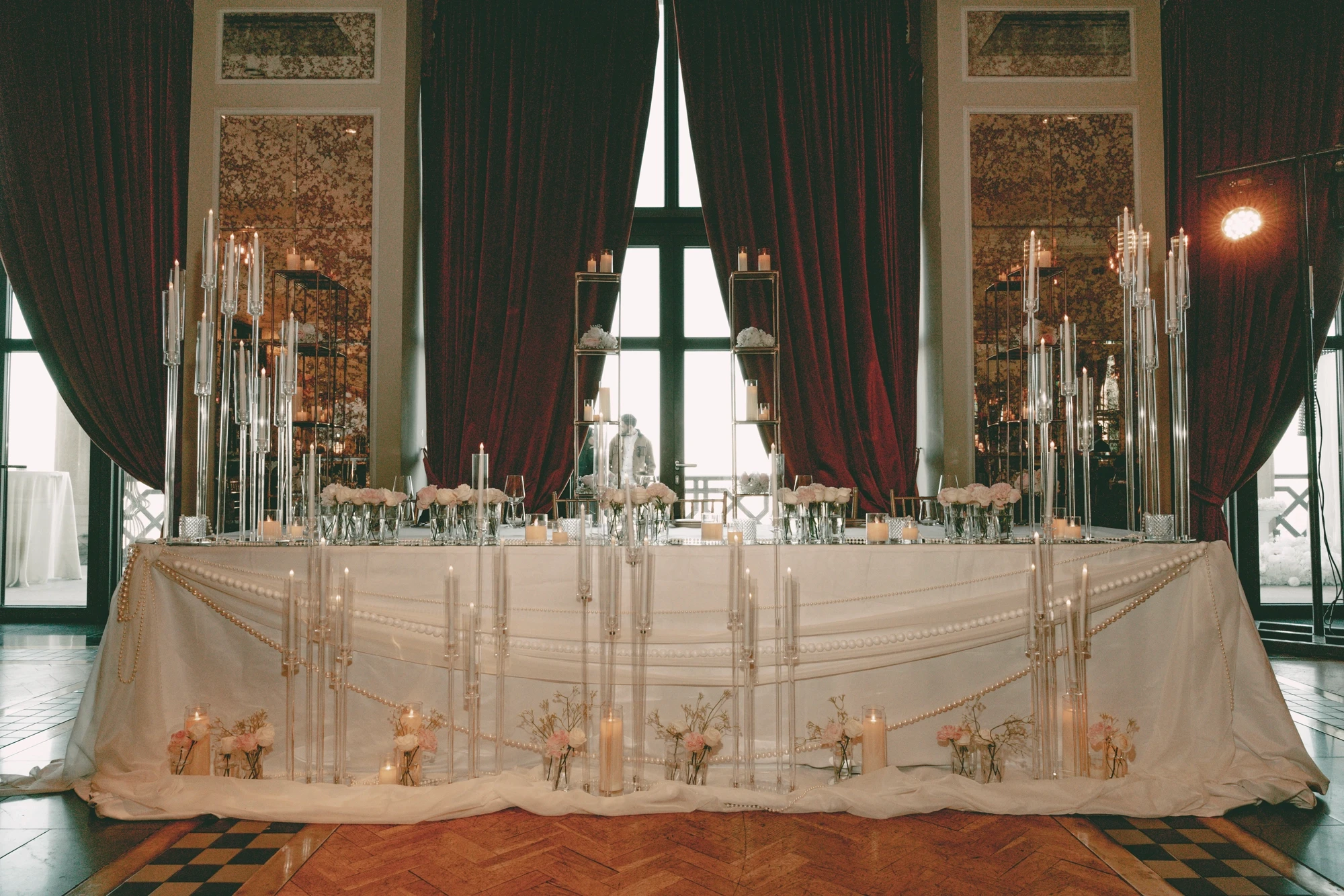 ელეგანტური ქორწილის პრეზიდიუმი მაღალი მინის სანთლებით, თეთრი ქსოვილითა და ნაზი ყვავილებით მდიდრულ სივრცეში