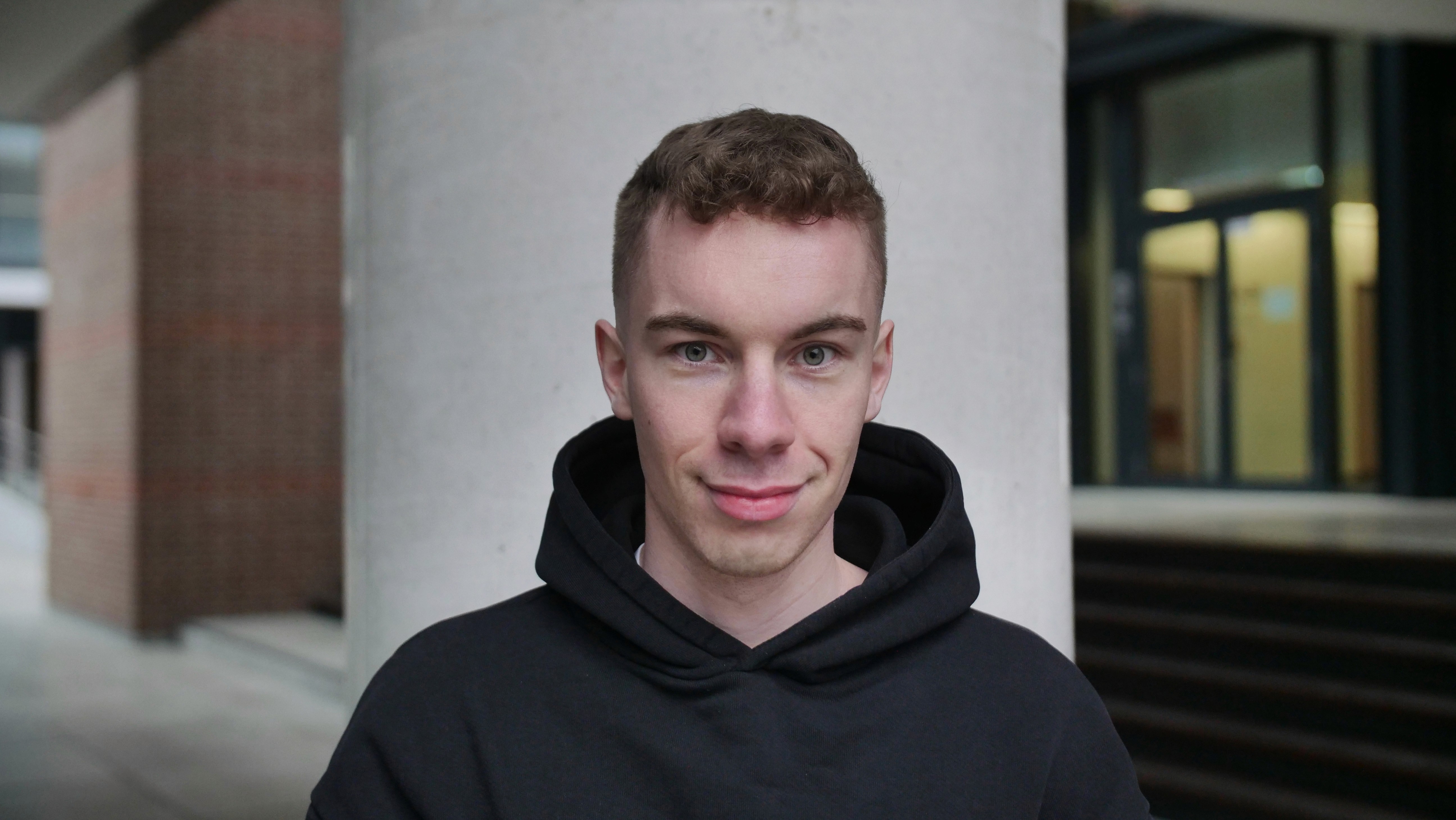A woman with long dark hair wearing a black hijab, looking calmly at the camera against a muted background.