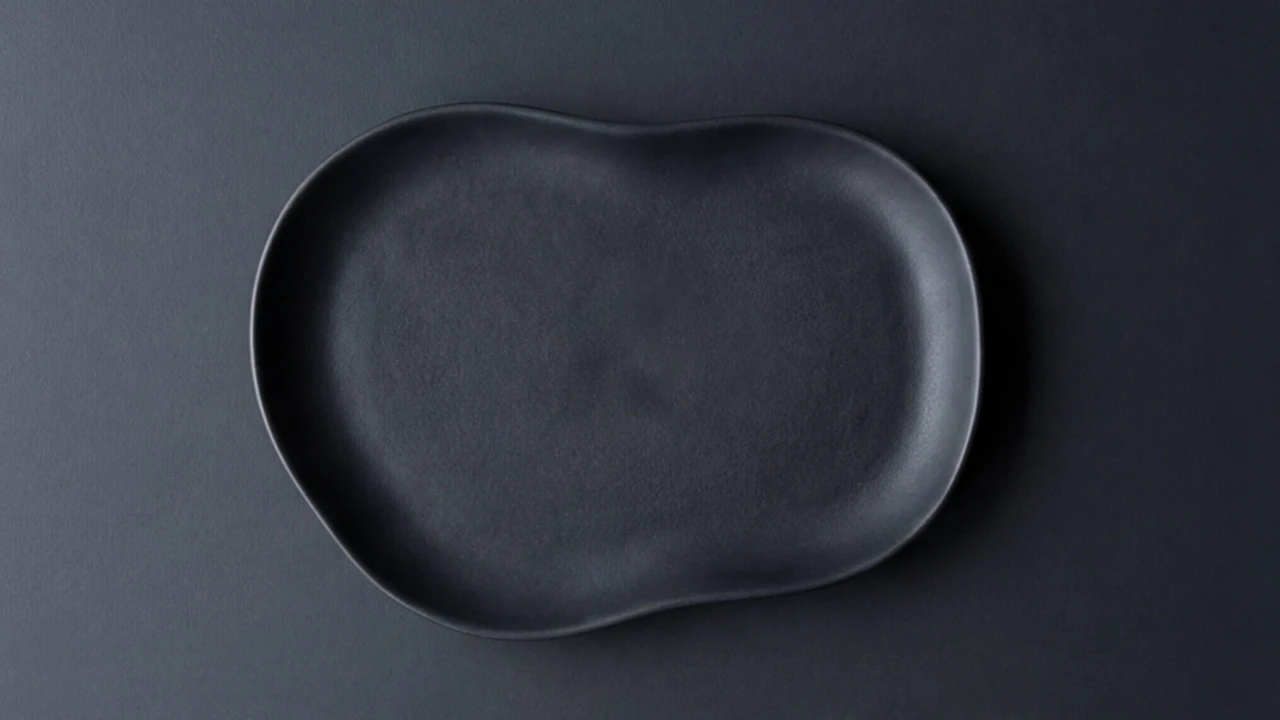 A matte black, organically shaped decorative tray resting on a dark grey geometric block.
