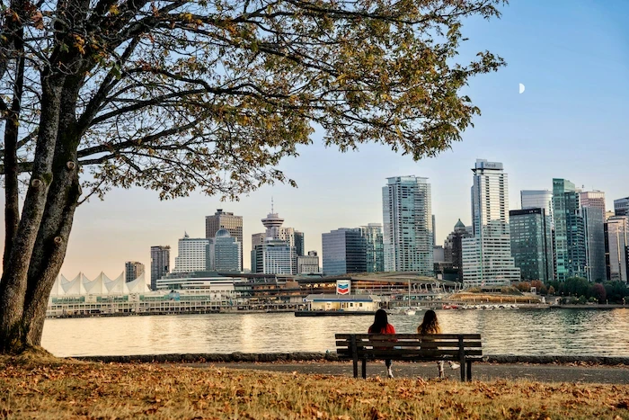 People sitting on a park bench in Stanley Park facing Vancouver’s waterfront skyline at sunset.