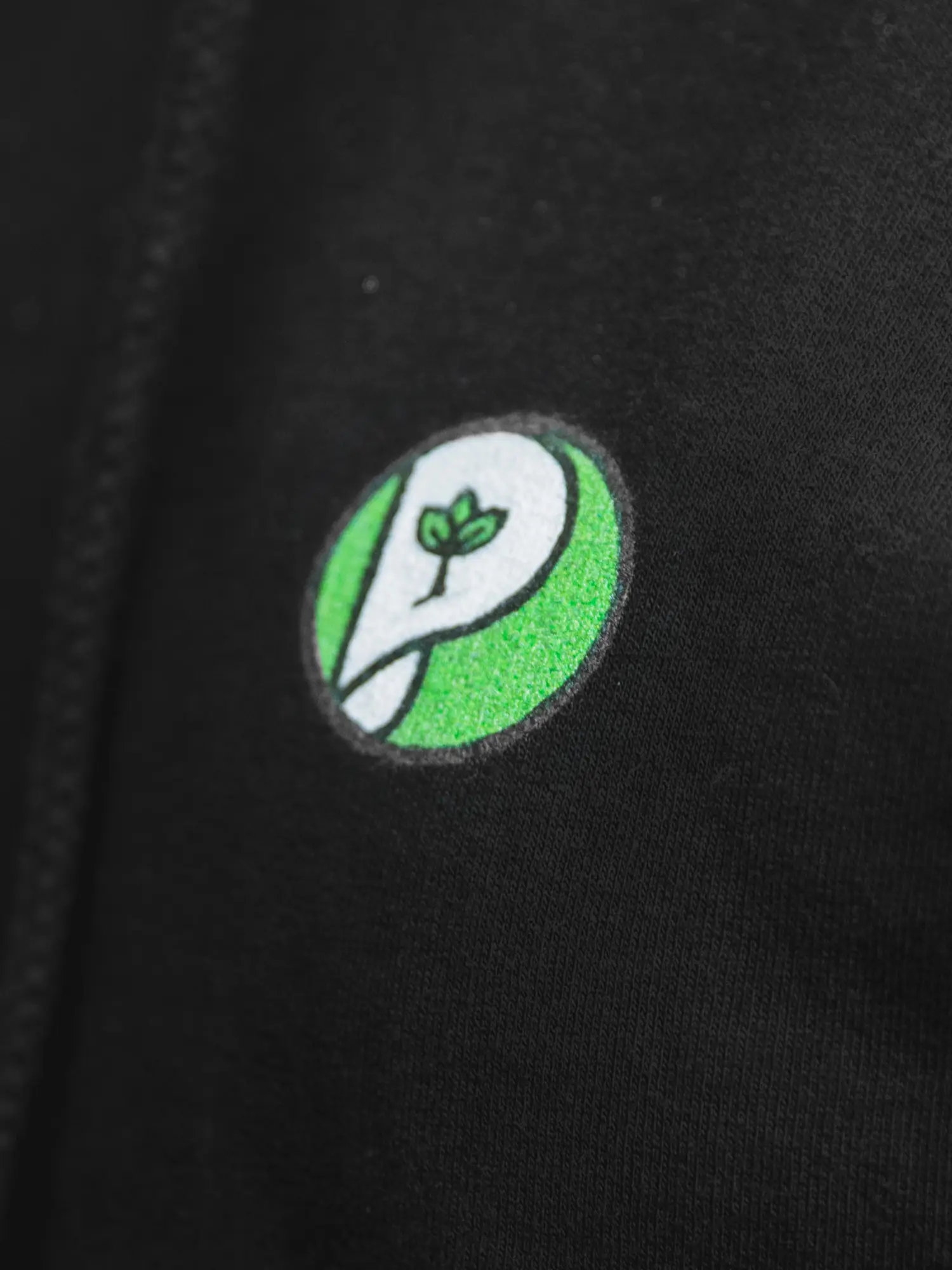 Aufgenähtes rundes Printzipia-Logo mit P und Blatt auf schwarzer Kleidung