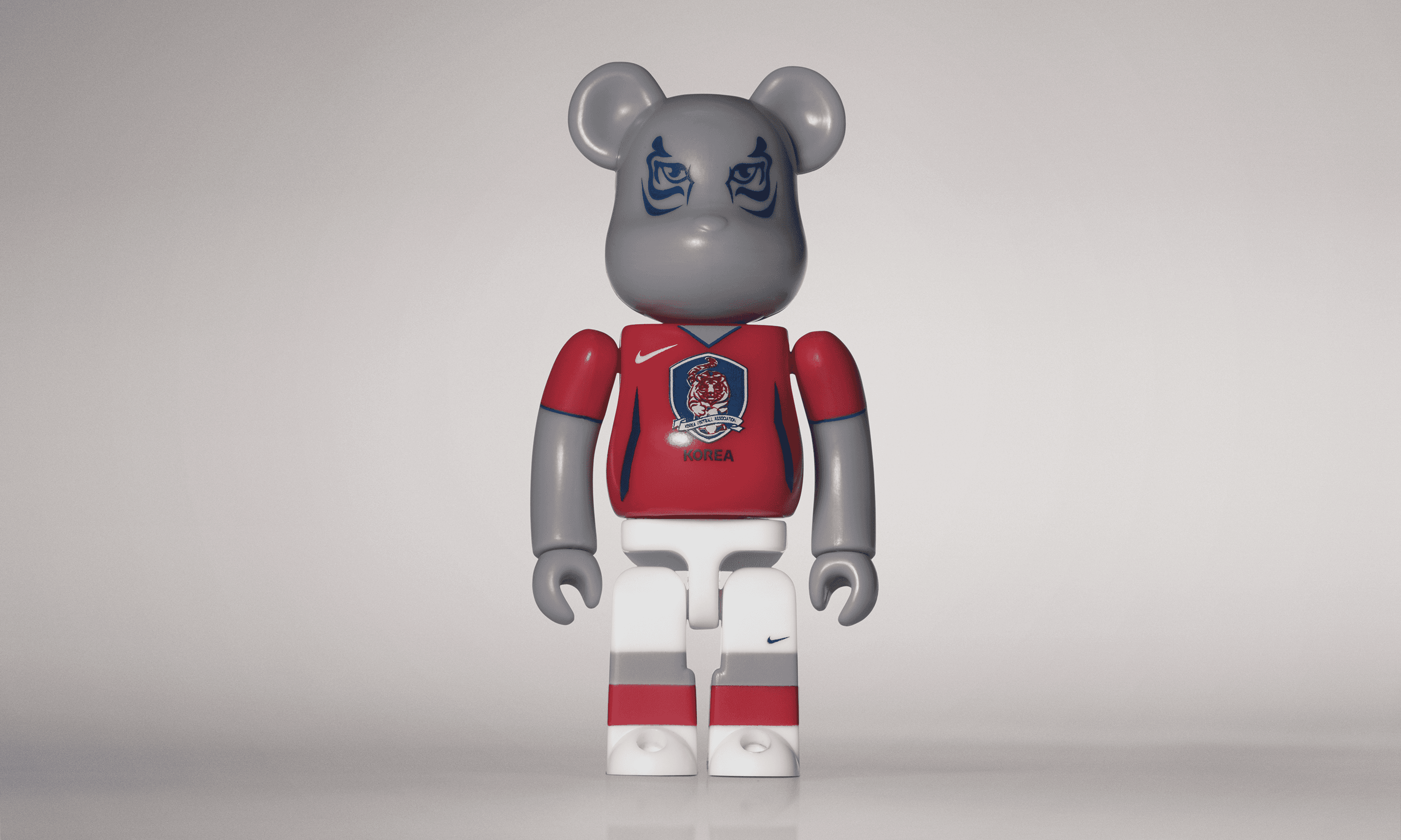 A single 3.5” tall Bre@rbrick/Nike toy created to commemorate the 2006 South Korean World Cup football team. The toy is painted to appear in the South Korean football kit and stands in the center of the frame in front of a white and grey background. 