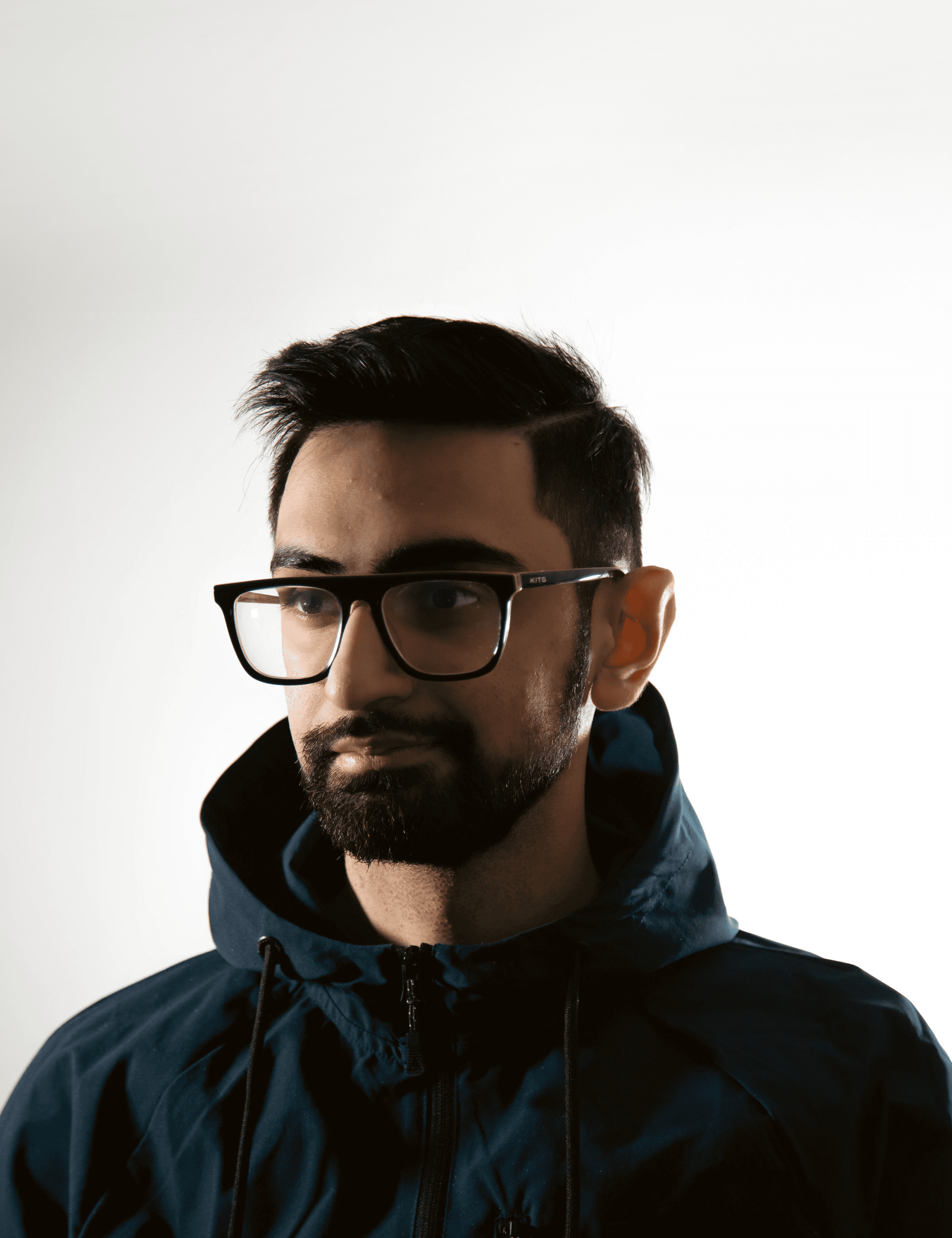 A man in a brown suit and cream silk scarf poses against a neutral background, exuding a composed and sophisticated demeanor.
