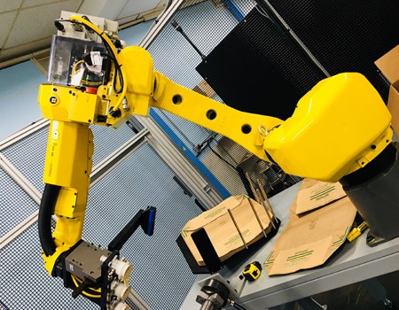 Automated picking robot working inside Kirin Group's Ebina distribution center, surrounded by inventory shelves.