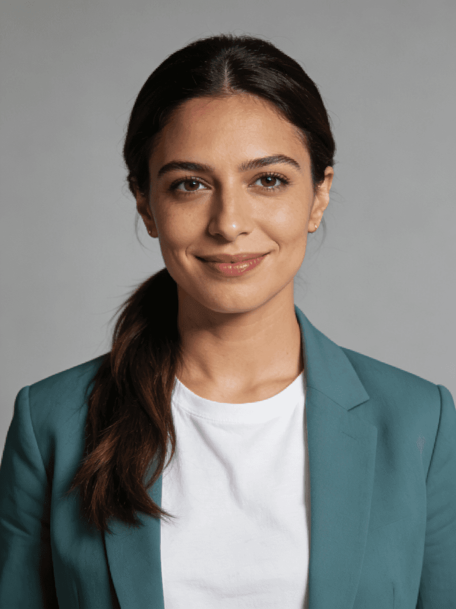 Smiling woman with dark hair in a ponytail, wearing a teal blazer and white t-shirt against a grey background.