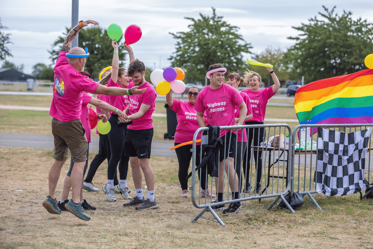 Outdoor team-building event with participants wearing matching blue shirts, taking part in inflatable obstacle courses and games, smiling and cheering, with the words 'ENTER A TEAM' in large bold white and green text across the image.