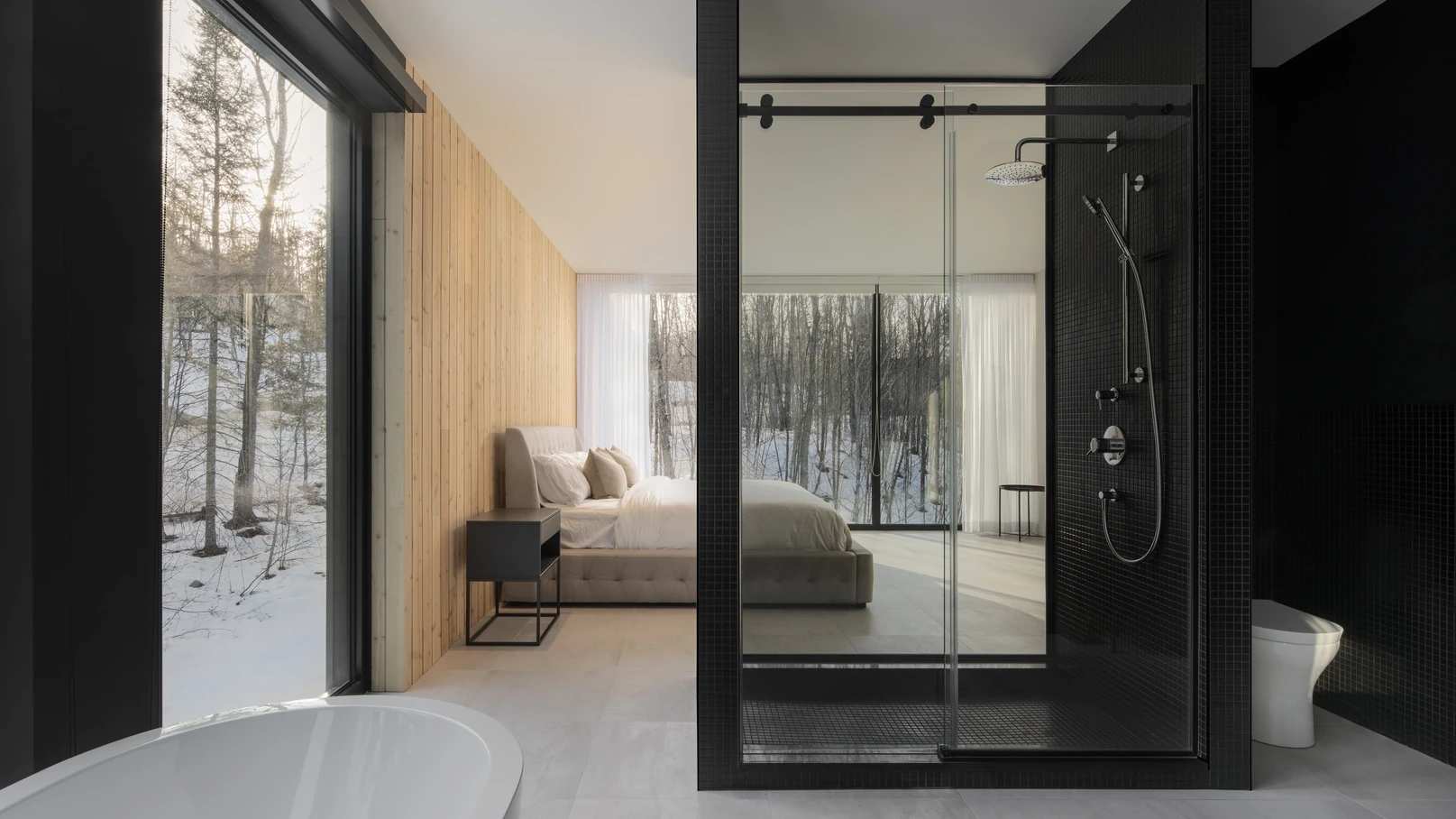 Master bedroom and open-concept bathroom – A soft, neutral-toned bedroom with a panoramic forest view, separated by a black glass-walled shower.