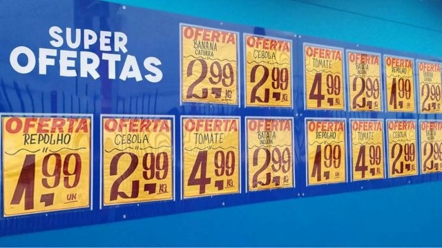 Painel azul com cartazes de promoção e ofertas de frutas e verduras.