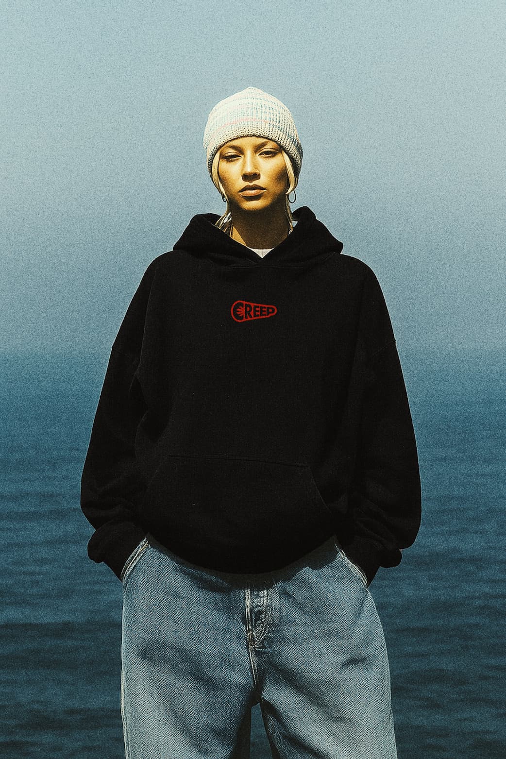 creep red wordmark on black hoodie worn by model stood on beach 