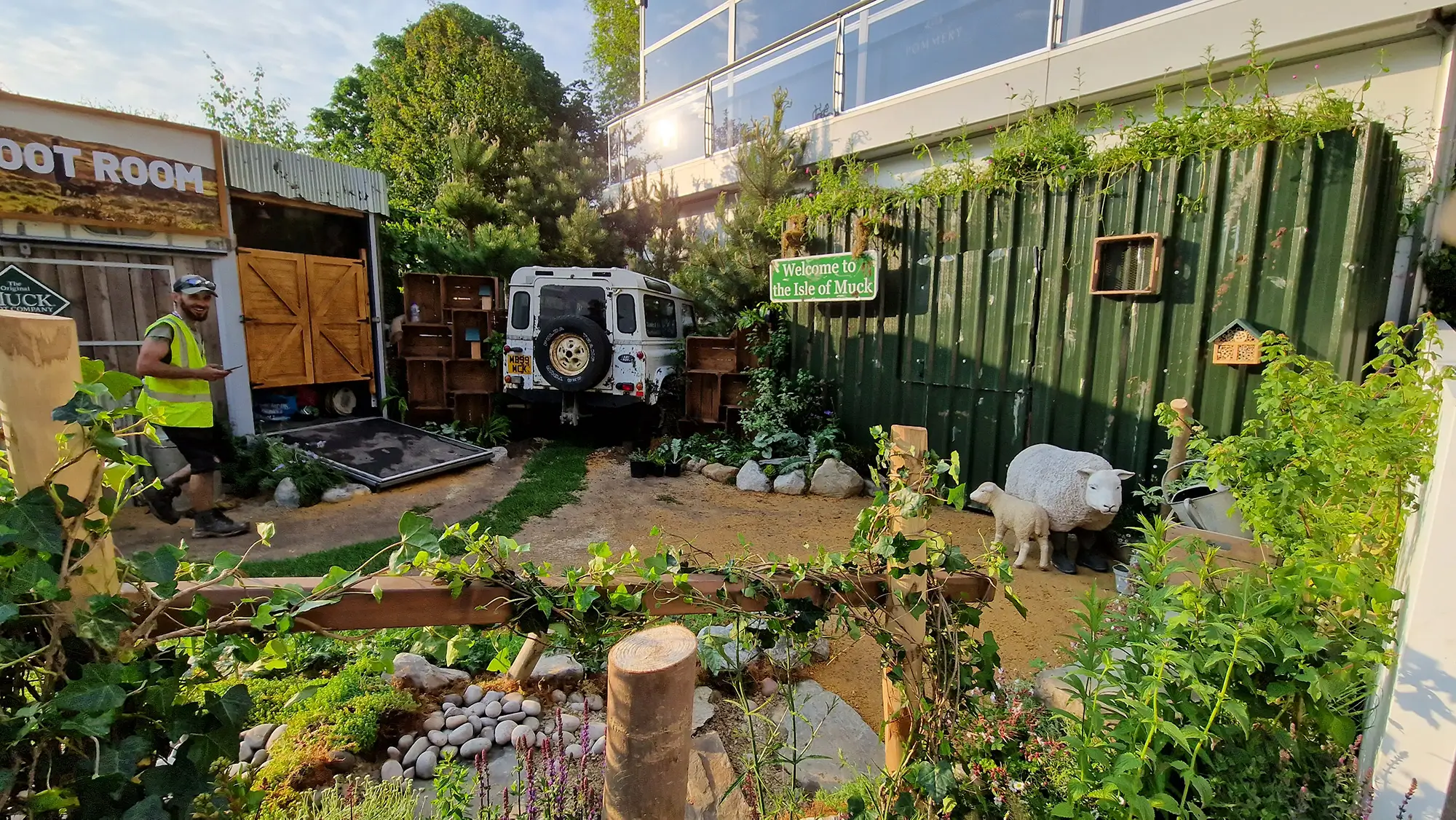 A vibrant garden scene featuring a variety of plants, a small pond, and wooden structures under a clear sky.
