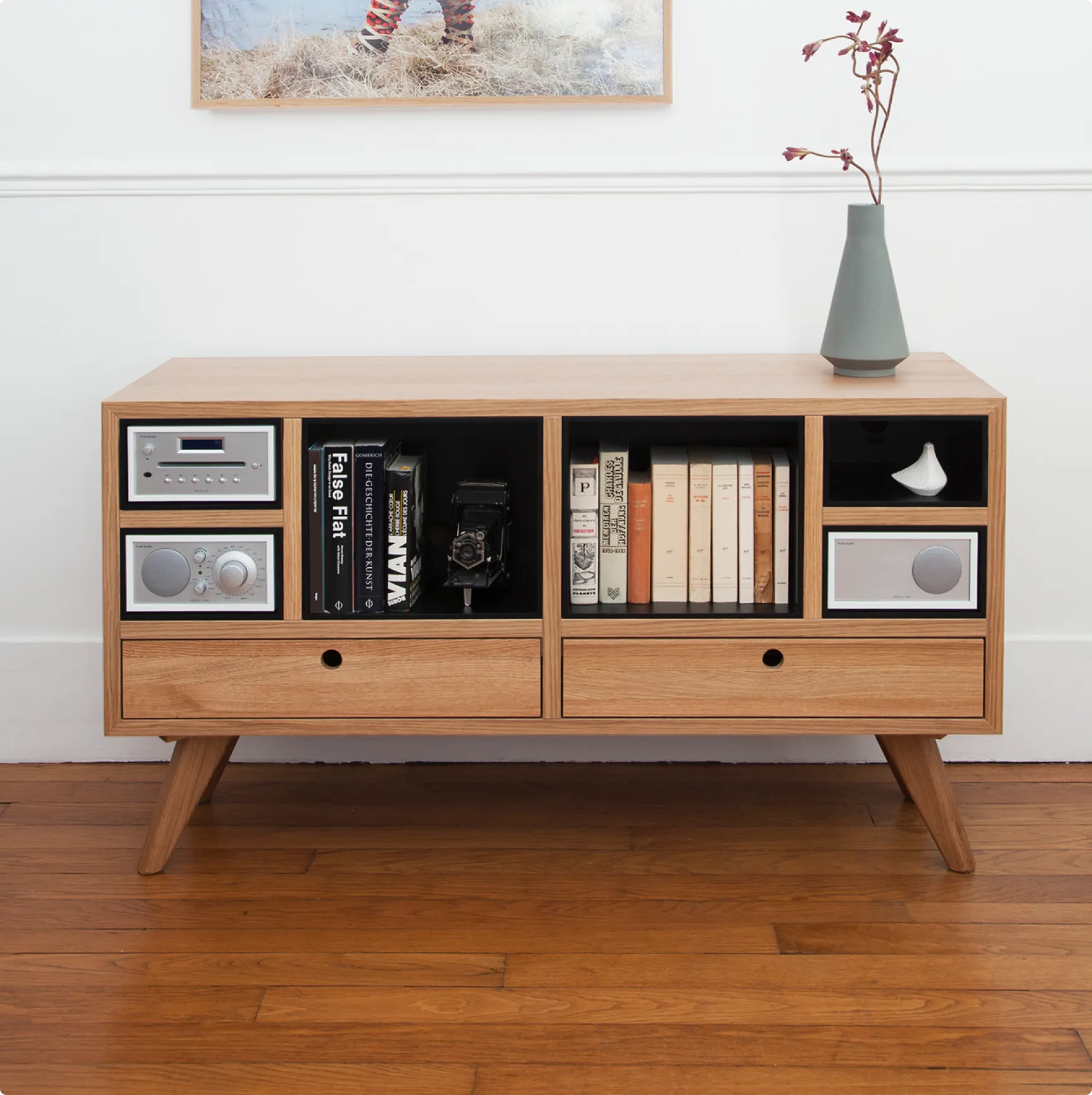 A wooden media console with open shelves and drawers, styled with decor and books against a white wall.